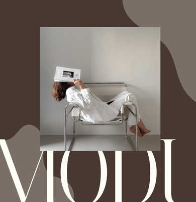 Zdjęcie z projektu graficznego MODU – kobieta w białym stroju leżąca na metalowym krześle, trzymająca magazyn, na tle minimalistycznego wnętrza z napisem MODU. Przykład eleganckiego brandingu stworzonego przez Patie Projektuje.